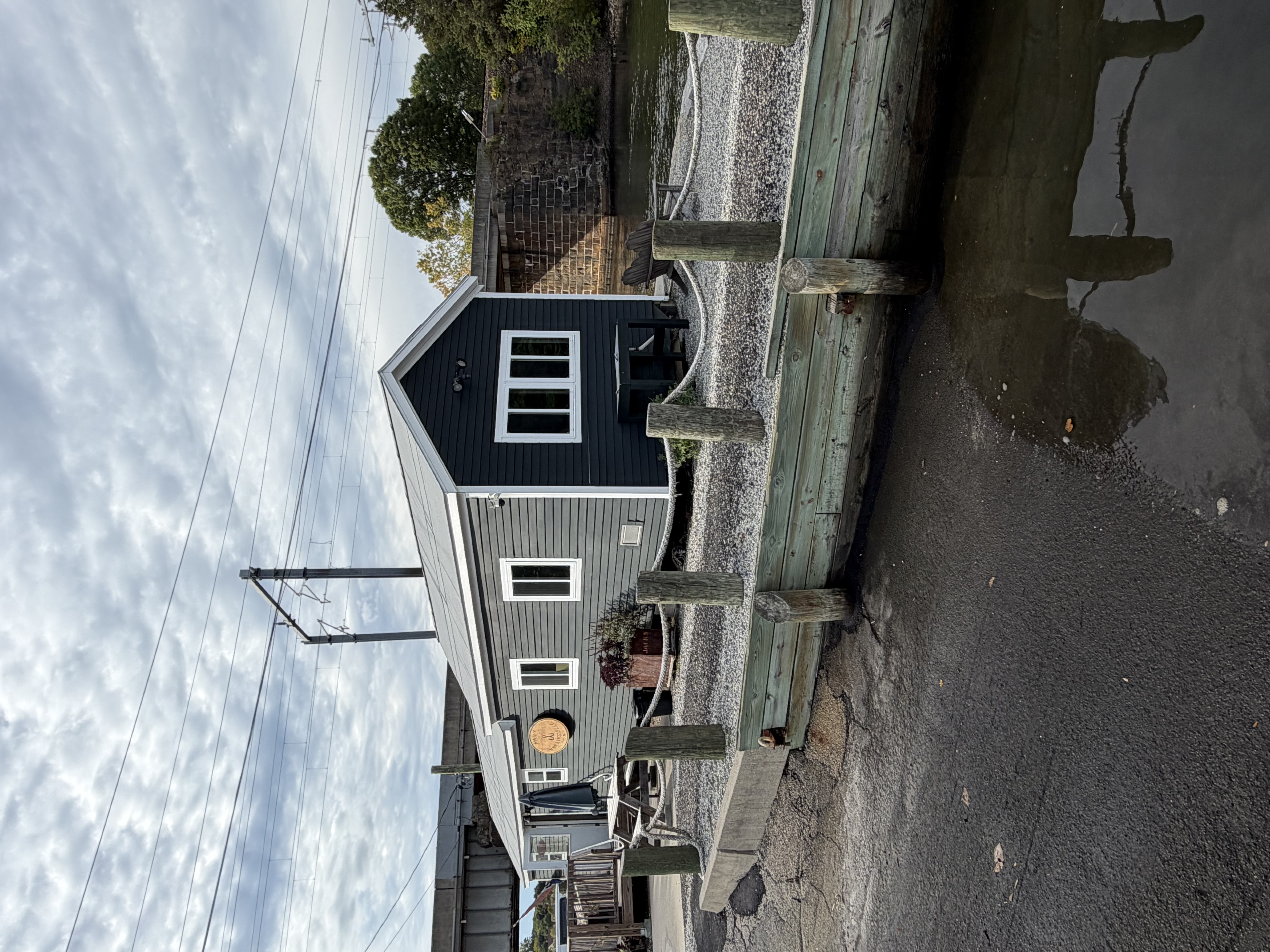 A gray shingled fishing shanty standing on pilings over the water at Apponaug Cove, rope railing along its deck